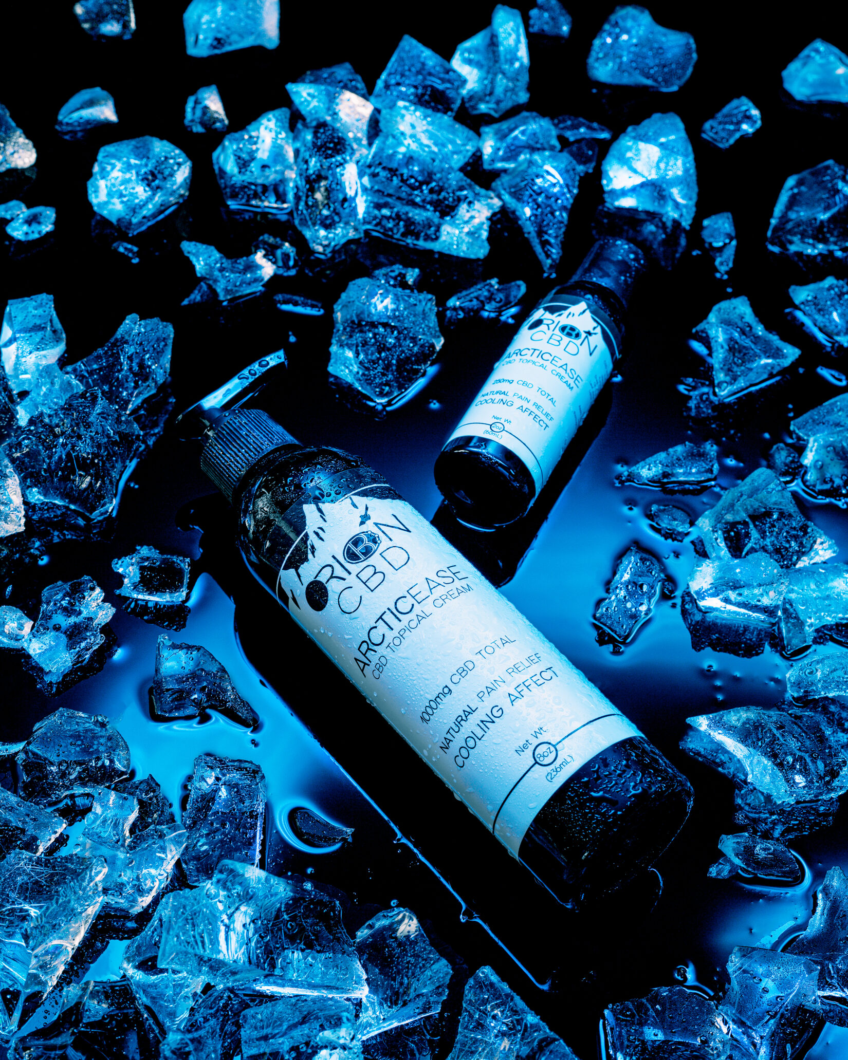Two Arctic Ease CBD topical cream bottles by Orion CBD on a liquid black surface among ice, with blue cooling lighting.